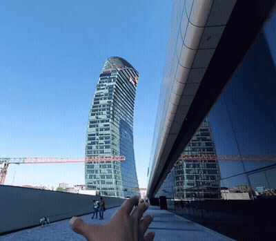 A Hand Reaches Up Towards A Tall Building With A Blue Sky In The Background GIF