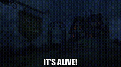 A Haunted House Is Lit Up At Night With The Words `` It 'S Alive '' Written In White Letters . GIF