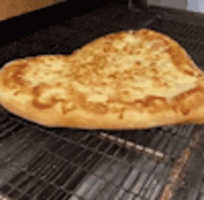 A Heart Shaped Pizza Is Sitting On A Wire Rack On A Grill . GIF