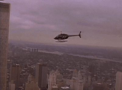 A Helicopter Is Flying Over A City With A Few Buildings In The Background GIF