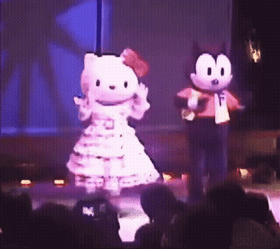 A Hello Kitty Mascot And Felix The Cat Mascot Are Dancing On A Stage In Front Of A Crowd . GIF