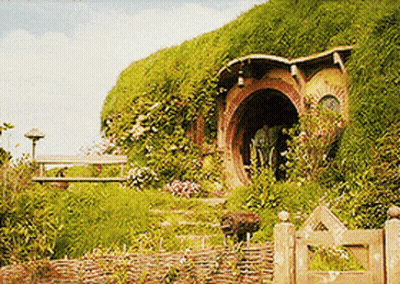 A Hobbit House Sits On Top Of A Hill With A Wooden Gate In Front Of It GIF