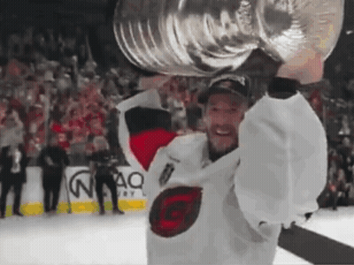 A Hockey Player Holds A Trophy Over His Head In Front Of A Crowd GIF