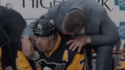 A Hockey Player Is Being Helped By A Man In A Suit While Sitting On A Bench . GIF