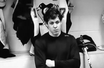 A Hockey Player Is Standing In A Locker Room With His Arms Crossed And A Hockey Stick . GIF