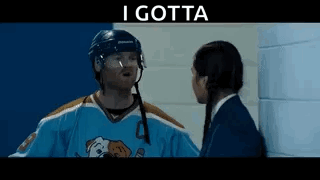 A Hockey Player Is Talking To A Girl In A Locker Room While Wearing A Blue Jersey With A Dog On It . GIF