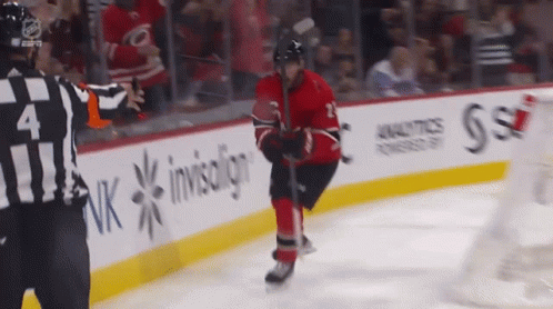 A Hockey Player Stands On The Ice With A Referee In Front Of A Banner That Says Invisalign GIF