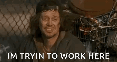 A Homeless Man Is Sitting In Front Of A Chain Link Fence And Says `` Im Tryin To Work Here '' . GIF