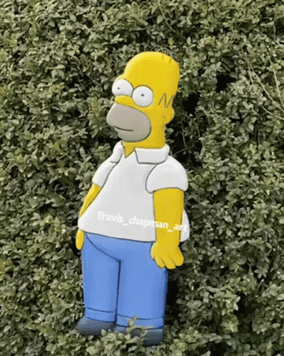 A Homer Simpson Statue Is Standing In A Bush GIF