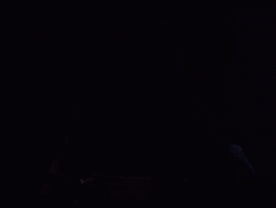 A Hooded Figure In A Dark Room With A Red And Black Mask GIF