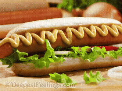 A Hot Dog On A Bun With Mustard And Lettuce On A Table GIF