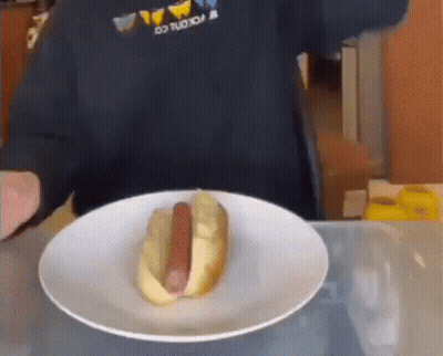 A Hot Dog On A Plate With A Person Behind It GIF