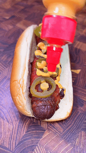 A Hot Dog With Jalapenos And Mustard Is Being Poured On It GIF
