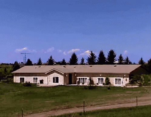 A House Sits In The Middle Of A Grassy Field With Trees In The Background GIF