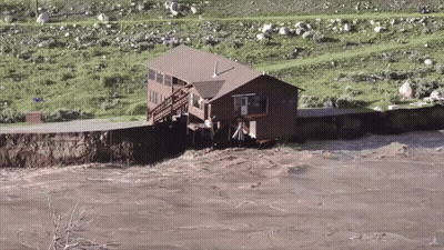A House Sits In The Middle Of A River Surrounded By Grass And Rocks GIF
