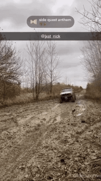 A Jeep Is Driving Down A Muddy Road With Trees In The Background GIF