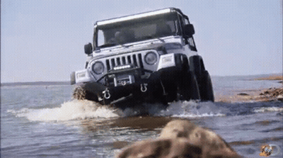 A Jeep Is Driving Through A Body Of Water With A Few Rocks In The Foreground GIF