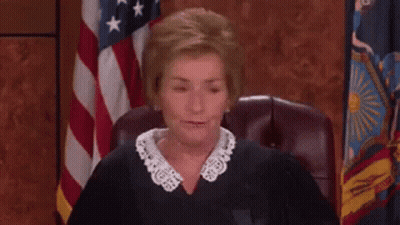 A Judge Is Sitting In A Courtroom With An American Flag In The Background . GIF