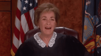 A Judge Is Sitting In Front Of An American Flag And Smiling . GIF