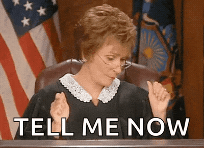 A Judge Sitting In Front Of An American Flag With The Words Tell Me Now Written Below Her GIF