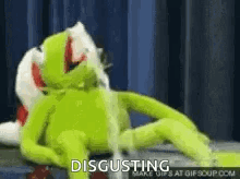 A Kermit The Frog Is Laying On A Bed With A Stuffed Animal And Says `` Disgusting '' . GIF