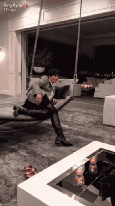 A King Kylie Snapchat Shows A Woman Sitting On A Swing In A Living Room GIF