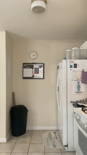 A Kitchen With A Clock On The Wall Above The Refrigerator And A Bulletin Board On The Wall GIF