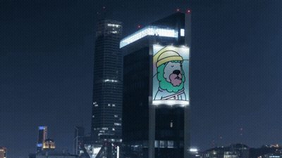 A Large Billboard On The Side Of A Building Has A Picture Of A Man With A Beard And Hat On It GIF
