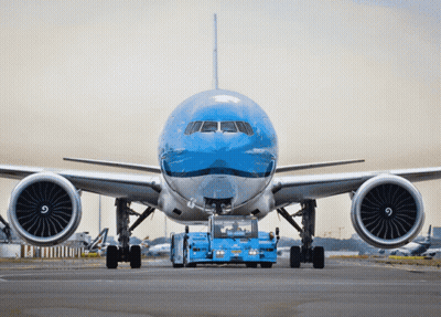 A Large Blue And White Airplane Is Being Towed By A Blue Vehicle GIF