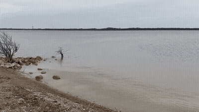 A Large Body Of Water With Rocks And Trees In The Foreground GIF