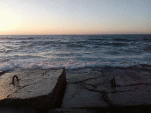 A Large Body Of Water With Waves Crashing On A Rocky Shoreline GIF