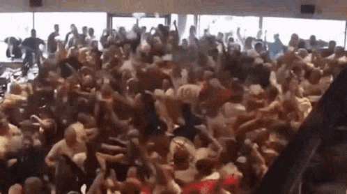 A Large Crowd Of People Are Dancing In A Room With A Lot Of Windows . GIF