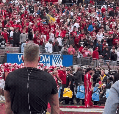 A Large Crowd Of People Watching A Football Game In Front Of A Sign That Says Wom GIF