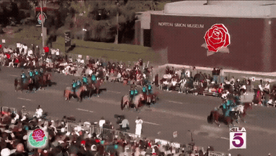 A Large Crowd Of People Watching A Parade In Front Of A Building That Says Norton Simon Museum GIF