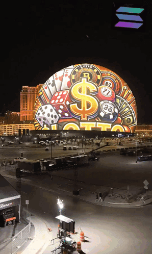 A Large Globe With A Dollar Sign Dice And Playing Cards On It Is Lit Up At Night GIF