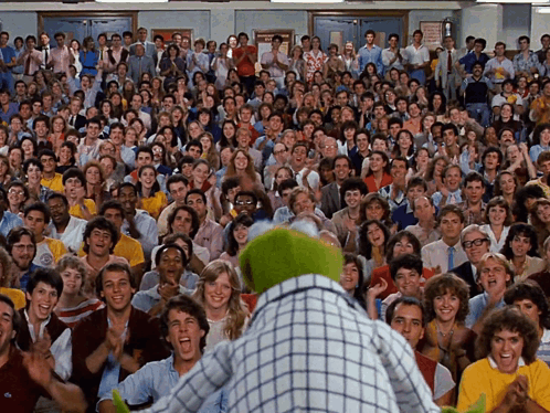 A Large Group Of People Are Gathered In A Room With A Sign That Says No Smoking GIF