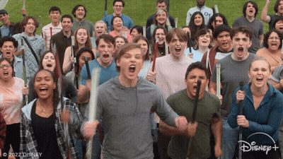 A Large Group Of People Are Holding Bats And Screaming In Front Of A Disney+ Logo GIF
