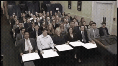 A Large Group Of People Are Posing For A Picture And One Of Them Is Holding A Piece Of Paper GIF