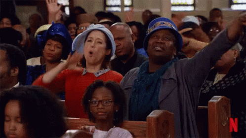 A Large Group Of People Are Sitting In A Church With Their Hands In The Air . GIF