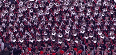 A Large Group Of People Are Standing In A Stadium Playing Instruments . GIF