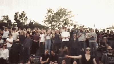 A Large Group Of People Are Standing In A Stadium With Their Arms In The Air . GIF