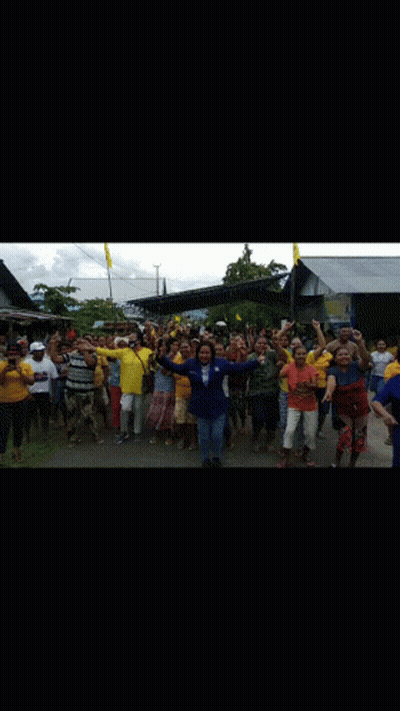 A Large Group Of People Are Standing In Front Of A Building Holding Their Hands Up In The Air . GIF