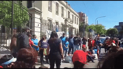 A Large Group Of People Are Standing In Front Of A Building On A Street . GIF