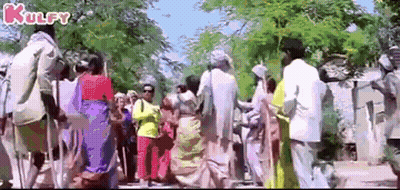 A Large Group Of People Are Walking Down A Street In A Village . GIF