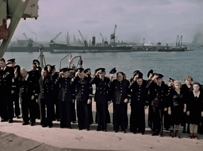 A Large Group Of People In Black Uniforms Salute In Front Of A Body Of Water GIF