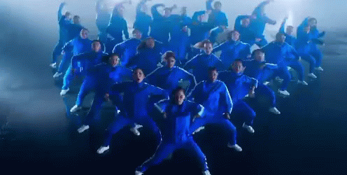 A Large Group Of People In Blue Jumpsuits Are Dancing GIF