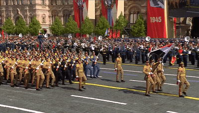 A Large Group Of Soldiers Marching Down A Street With A Banner That Says 1945 GIF