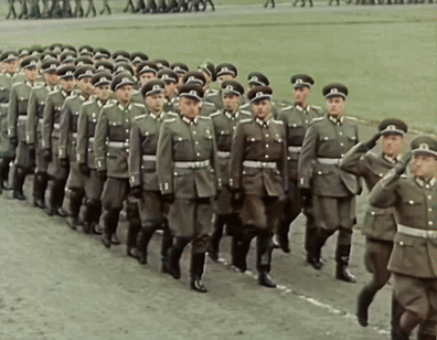 A Large Group Of Soldiers Marching In A Line With One Wearing A Hat With The Letter T On It GIF