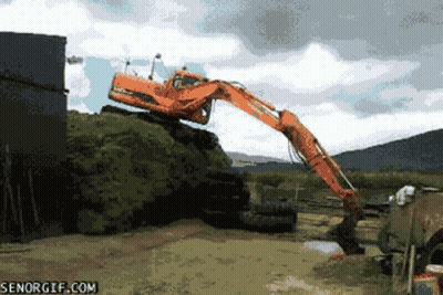 A Large Orange Excavator Is On Top Of A Pile Of Grass GIF