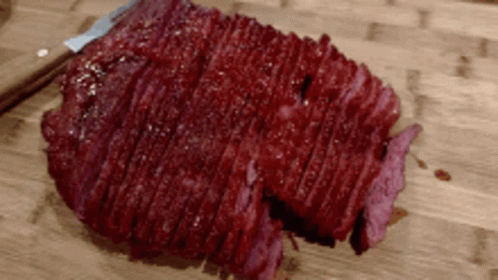 A Large Piece Of Meat Is Sitting On A Wooden Cutting Board GIF